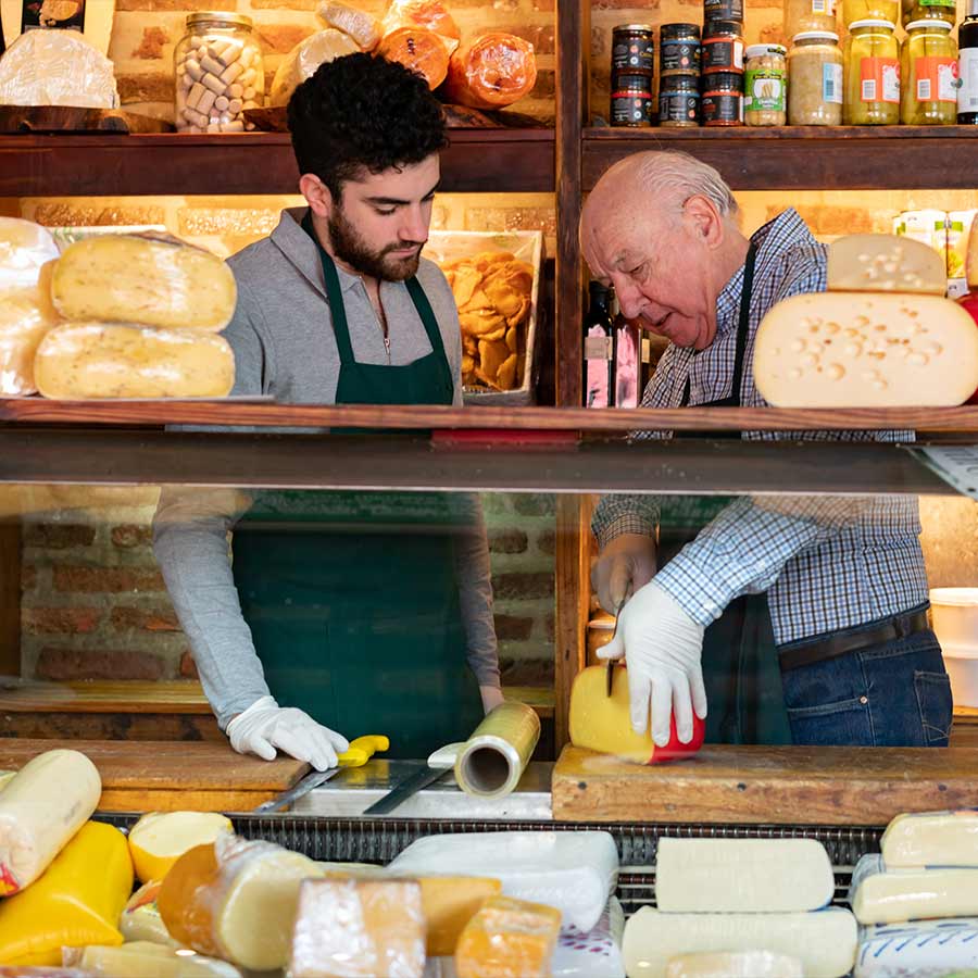 Señor mayor y joven cortando queso en una fiambrería