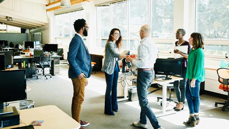 A group of people standing and one man is shaking the hand of woman. A group of people standing and one man is shaking the hand of woman.